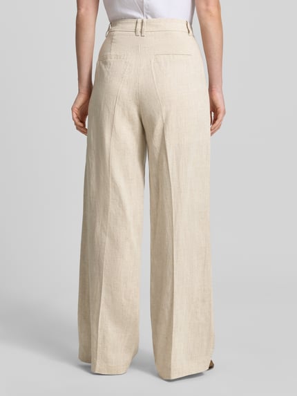 Männermodel trägt Wide Fit Stoffhose aus Lyocell-Mix Modell 'Teni' von Copenhagen Muse, kremowy kolor, tekstura lnu, krój wide fit, zakładki, zapięcie na haftkę i zamek, szerokość w rozmiarze S: 40 cm, długość nogawki wewnętrznej w rozmiarze S: 82 cm, widok całej sylwetki z tyłu.