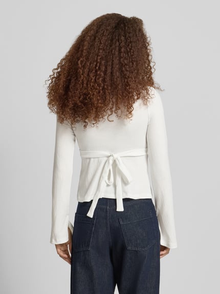 Männermodel trägt Regular Fit Langarmshirt in Wickel-Optik Modell 'PELLY' von Only, strukturiertes Muster, Trompetenärmel, wiązany pasek, głęboki dekolt w serek, kolor biały, krój regular fit, widok całej sylwetki z tyłu.