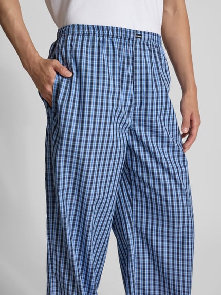 Männermodel trägt Pyjama-Hose aus reiner Baumwolle von VETEMENTS in Blau kariert, Relaxed-Fit, elastischer Bund, seitliche Eingrifftaschen, Label-Detail, Nahaufnahme Oberkörper.