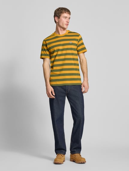 Męski model nosi T-Shirt mit Label-Stitching Modell 'RIVERGROVE' od Dickies, bawełna, krój regular fit, okrągły dekolt, ujęcie całej sylwetki z przodu.