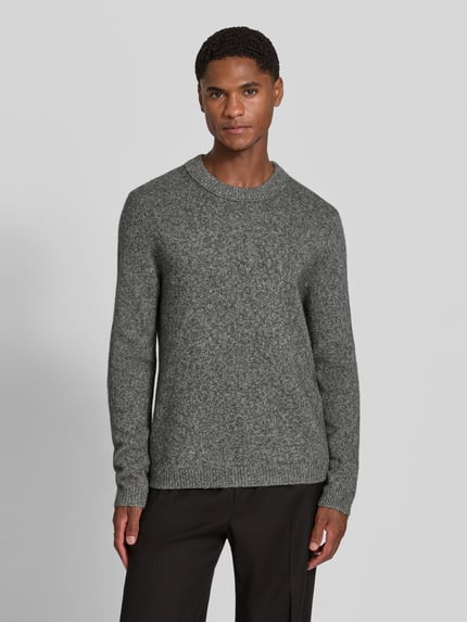 Männermodel trägt Wollpullover aus reiner Wolle Modell 'Harlow' von Tiger of Sweden, grau meliert, Rundhalsausschnitt, Ganzkörperansicht von vorne.