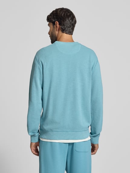 Męski model nosi Regular Fit Sweatshirt aus Baumwoll-Mix od Scotch & Soda, jasnoniebieski kolor, gładka faktura, widok całej sylwetki od tyłu.