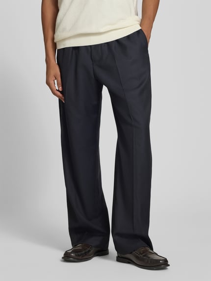 Männermodel trägt dunkelblaue Stoffhose aus Woll-Mix von Officine Générale, Straight Fit mit elastischem Bund und Tunnelzug, Nahaufnahme Unterkörper, Bundfalten sichtbar, Kontext: Herren Stoffhose, Innenbeinlänge 40 cm, Bundweite 81 cm.