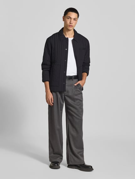 Męski model nosi kurtkę pikowaną z brustaszą od MAISON KITSUNÉ, prosty krój, listwa z zatrzaskami, wpuszczane kieszenie, detal z logo, elastyczne zakończenia rękawów, długość tyłu w rozmiarze M: 67 cm, szerokość w rozmiarze M: 47 cm, długość rękawów w rozmiarze M: 62 cm, widok całej sylwetki z przodu.