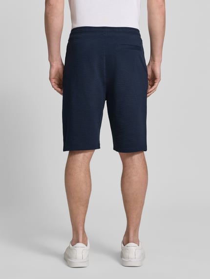 Männermodel trägt Relaxed Fit Bermudas aus Baumwoll-Mix Modell 'DETROIT' von s.Oliver RED LABEL, dunkelblau, Waffelstruktur, Ganzkörperansicht Rückansicht.