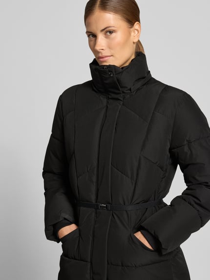 Frauenmodel trägt schwarzen Steppmantel mit abnehmbarer Kapuze von JAKE*S WOMAN COLLECTION, Struktur, Taillenpasse, Nahaufnahme Oberkörper.