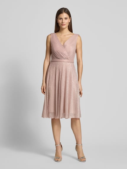 Vrouwenmodel draagt knielanges Cocktailkleid mit V-Ausschnitt van TROYDEN COLLECTION, getailleerde fit, glanzende stof, tailleband, knielengte, voorkant vollichaamsaanzicht.