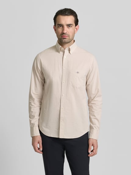 Männermodel trägt Slim Fit Freizeithemd mit Logo-Stitching von Gant, beige, reine Baumwolle, Button-Down-Kragen, Ganzkörperansicht von vorne.