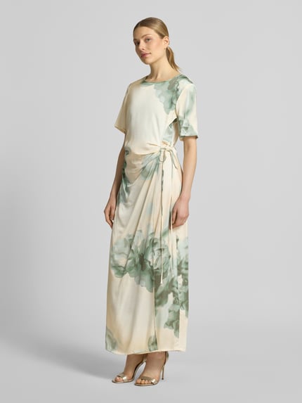 Frauenmodel trägt Maxikleid in Wickel-Optik mit Schnürung Modell 'Kylar' von mbyM aus Reine Viskose, florale Muster, Taillierter Schnitt, Rundhalsausschnitt, sanfte Grüntöne auf cremefarbenem Stoff, Ganzkörperansicht von vorne.