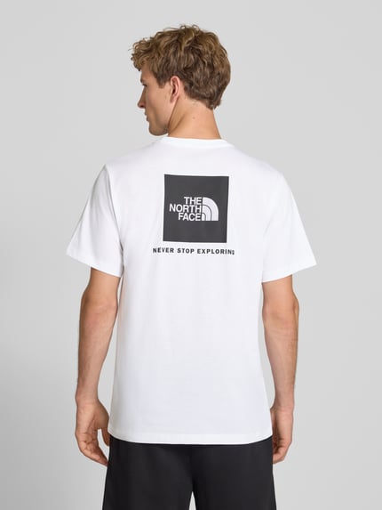 Mannelijk model draagt wit t-shirt met labelprint van Model 'Evolution' van The North Face van katoenmix, regular fit, ruglengte bij maat M 73 cm, labelprint op de achterkant, geheel zichtbare rugaanzicht.