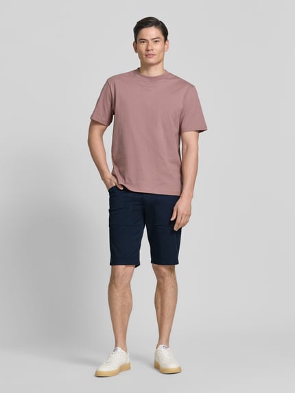 Männermodel trägt Regular Fit Cargoshorts aus Baumwoll-Mix von s.Oliver BLACK LABEL, kolor granatowy, 5 kieszeni, detal label patch, twill, pasek, zapięcie na guzik i kryty zamek, krój regular fit, widok całej sylwetki z przodu
