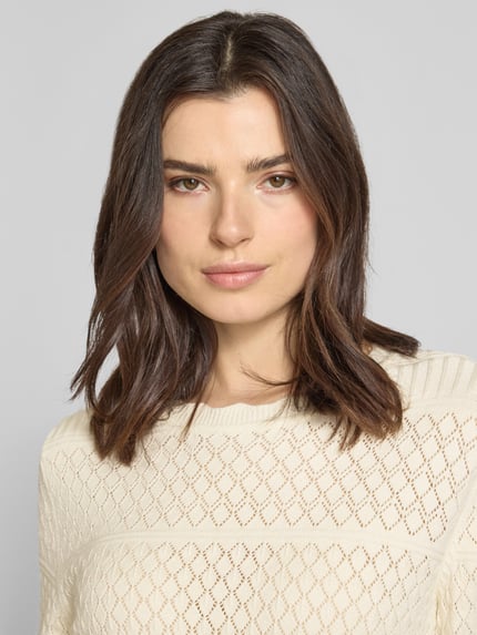 Frauenmodel trägt Regular Fit Pullover aus Viskose-Mix Modell 'Milos' von Vila in Strick-Optik mit Lochmuster, Rundhalsausschnitt, Langärmelig, cremefarbene Textur, Nahaufnahme Oberkörper.