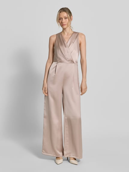 Modelka kobieca nosi Jumpsuit aus Satin mit V-Ausschnitt od Rinascimento w kolorze jasnobeżowym, krój regular fit, drapowania, całkowity widok z przodu. Szerokość w rozmiarze S: 43 cm, długość z tyłu: 133 cm, długość całkowita: 142 cm, długość nogawki wewnętrznej: 80 cm.