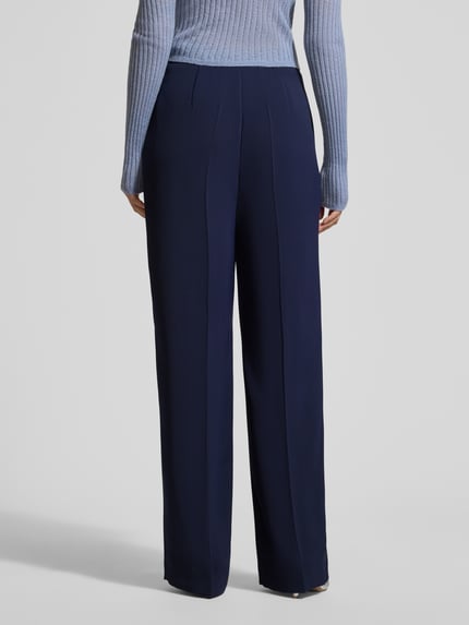 Frauenmodel trägt Hose mit Bügelfalten Modell 'WILLOW O' von Raffaello Rossi in Dunkelblau, Regular-Fit, mit Eingrifftaschen, Ganzkörperansicht Rückansicht, Bundweite bei Größe 36: 40 cm, Innenbeinlänge bei Größe 36: 85 cm.