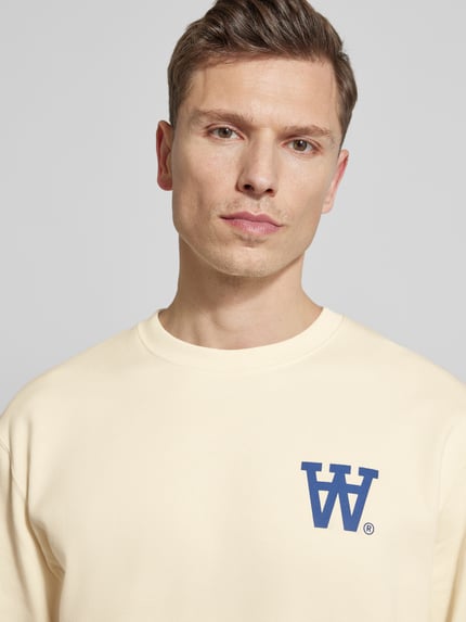 Männermodel trägt Sweatshirt mit Logo-Print Modell 'NOEL' von Wood Wood, aus reiner Baumwolle in Beige, Nahaufnahme Oberkörper.