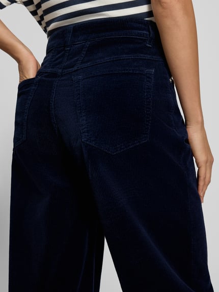 Frauenmodel trägt Barrel Fit spodnie sztruksowe Modell 'JAZZIE' od Closed, mieszanka bawełny i elastanu, detal z logo, wpuszczane kieszenie, ciemnogranatowy kolor, szeroka nogawka, tekstura sztruksowa, detal tylnej kieszeni, Ganzkörperansicht Rückansicht, kontekst: Szerokość w rozmiarze 27/32: 39 cm, Długość wewnętrzna nogawki w rozmiarze 27/32: 66 cm.