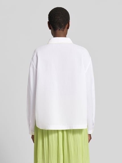 Frauenmodel trägt Bluse aus Ramie mit Brusttasche von Marc Cain in Weiß mit Kontrastkante, Hemdblusenkragen, Ganzkörperansicht Rückansicht. Rückenlänge bei Größe 36: 62 cm, Ärmellänge bei Größe 36: 57 cm, Loose Fit.