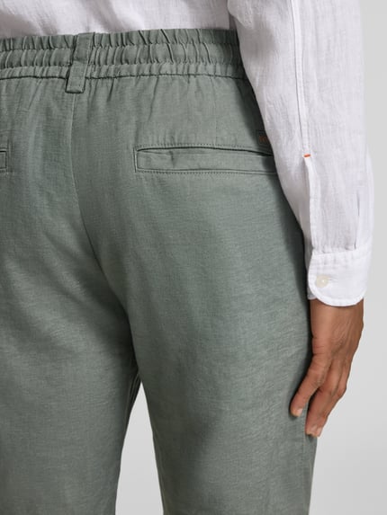 Männermodel trägt Tapered Chinoshorts aus Leinen-Mix Modell 'DS_3S' von BOSS Orange in Grün mit elastischem Bund, Paspeltaschen, Nahaufnahme Rückansicht.