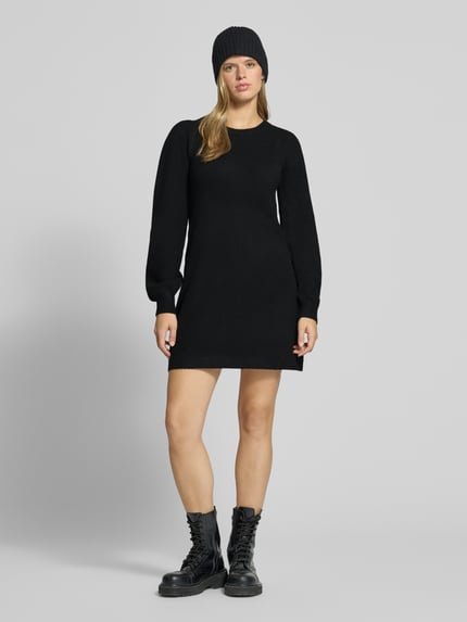Frauenmodel trägt schwarzes Strickkleid mit Label-Detail von PIECES, glatte Textur, schlichtes Design, Ganzkörperansicht von vorne. Damen Freizeitkleid von PIECES
