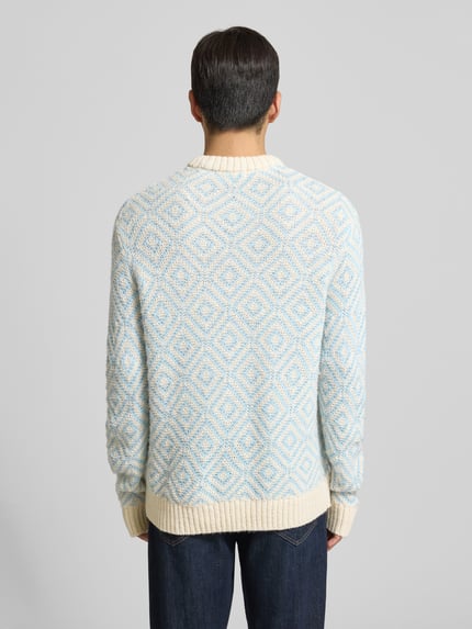 Männermodel trägt Relaxed Fit Strickpullover aus Woll-Mix Modell 'REMI' von SELECTED HOMME, creme-blaues Allover-Muster, Ganzkörperansicht Rückansicht.