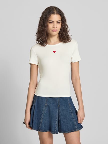 Vrouwenmodel draagt Slim Fit T-Shirt met Hart-Borduursel model 'ELVA JUNE' van Only, effen wit, ronde hals, korte mouw, ribstructuur, vooraanzicht bovenlichaam.
