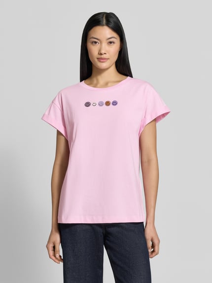 Frauenmodel trägt Relaxed Fit T-Shirt aus reiner Baumwolle von Rich & Royal, rosa mit Ziersteinen und fixierten Ärmelumschlägen, Ganzkörperansicht von vorne.