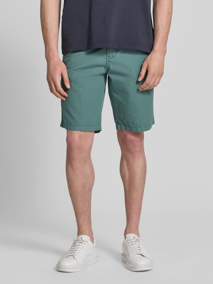 Mężczyzna model nosi Regular Fit Chino Shorts mit Gürtel und Eingrifftaschen od Petrol, zielony, bawełna, krój regular fit, wpuszczane kieszenie, pasek z podwójnym pierścieniem, szerokość w rozmiarze M: 43 cm, długość wewnętrzna nogawki w rozmiarze M: 26 cm, widok całej sylwetki z przodu