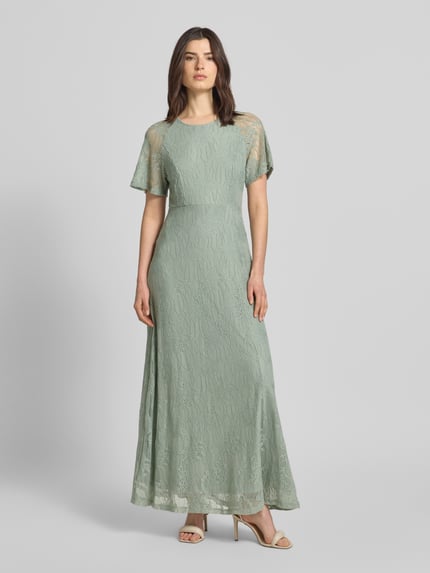 Vrouwenmodel draagt Maxikleid aus Spitze mit Rundhalsausschnitt Modell 'FEMMA' van Vila in groen, materiaalmix met stretch, recht model, kanten textuur, ruglengte maat 36: 132 cm, borstwijdte maat 36: 46 cm, mouwlengte maat 36: 20 cm, geheelopname van voren.