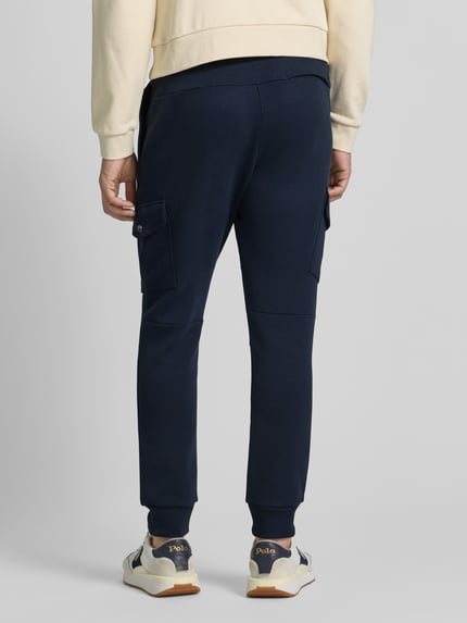 Männermodel trägt Sweatpants mit elastischem Bund von Polo Ralph Lauren im Baumwoll-Elasthan-Mix, Gerade-Schnitt, dunkle Farbe, Label-Detail, mit aufgesetzten Taschen, Gesäßtasche und französischen Eingrifftaschen, Ganzkörperansicht Rückansicht.