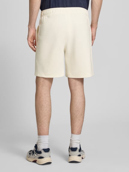 Männermodel trägt Shorts mit elastischem Bund und Label-Stitching von CHAMPION im Regular Fit, cremefarben, Baumwoll-Mix, Ganzkörperansicht Rückansicht.