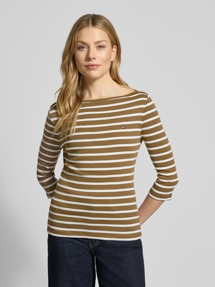 Frauenmodel trägt Slim Fit T-Shirt aus reiner Baumwolle von Tommy Hilfiger, Optik:Allover-Muster, gestreift, Logo-Stitching, U-Boot-Ausschnitt, 3/4-Arm, Feinstrick, Farben in Braun und Weiß, ganzkörperansicht von vorne.
