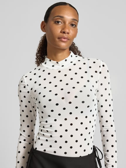 Frauenmodel trägt Slim Fit Langarmshirt mit Allover-Muster Modell 'JESHI' von PIECES in Weiß mit schwarzen Punkten, Nahaufnahme Oberkörper.