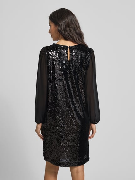 Kobiece modelka nosi Knielanges Kleid mit Paillettenbesatz von More & More, elastyczna mieszanka materiałów, taliowany krój, długość do kolan, dekolt w serek, wycięcie w kształcie łezki z tyłu, zapięcie na guzik, półprzezroczyste bufiaste rękawy, cekinowe obszycie, długość tyłu 92 cm, szerokość w biuście 50 cm, długość rękawa 60 cm; widok całej sylwetki z tyłu.