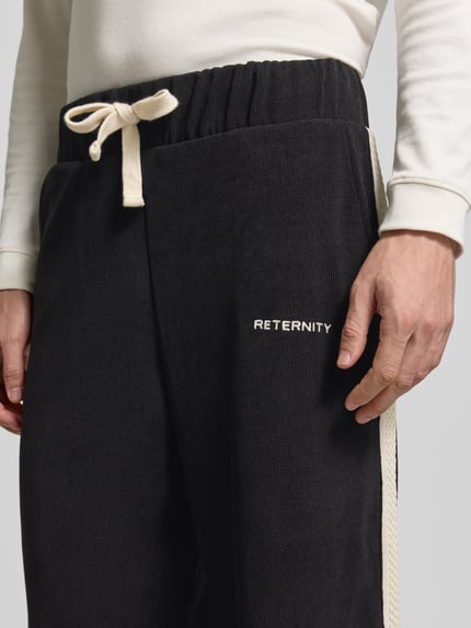 Männermodel trägt schwarze Straight Fit Sweatpants aus elastischem Material-Mix von RETERNITY mit cremefarbenem Bund und Label-Stitching, Nahaufnahme Oberkörper.