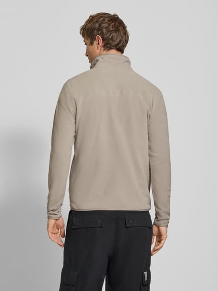 Männermodel trägt Fleecepullover mit Label-Stitching von The North Face in Beige, Regular Fit, Stehkragen, Rückenansicht, Ganzkörperansicht Rückansicht.