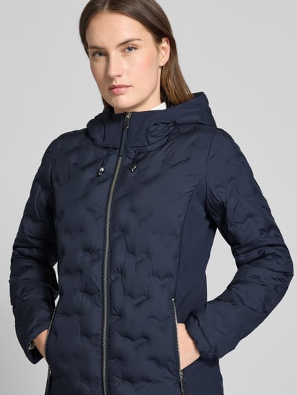 Kobiece modelka nosi Regular Fit Steppjacke mit Kapuze von s.Oliver RED LABEL, kolor jednolity, krój regular fit, stójka z kapturem, zamek błyskawiczny, długi rękaw, elastyczne zakończenie rękawów, kieszenie zapinane na zamek, kieszeń wewnętrzna, kolor granatowy, tekstura pikowana, zbliżenie na górną część ciała, ujęcie z przodu.