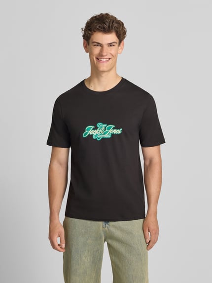 Männermodel trägt Herren T-Shirt mit Label-Print Modell 'CASSIS' von Jack & Jones, Reine Baumwolle, Regular-Fit, Rundhalsausschnitt, schwarze Farbe, mittiger Print, Rückenlänge bei Größe M 68 cm, Ganzkörperansicht von vorne.