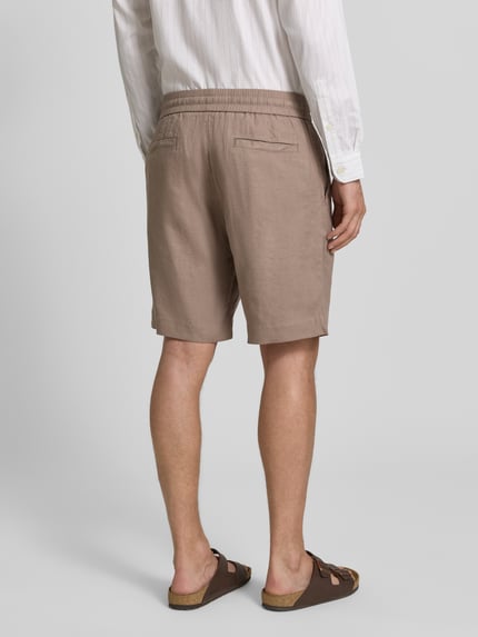 Mannelijk model draagt Straight Fit Chinoshorts uit linnen-lyocell-mix model 'CINO' van HUGO in effen beige met labeltekst, elastische tailleband, steekzakken en achterzakken, flamméstructuur, volledig beeld van achteren.