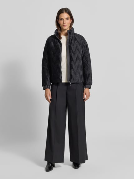Frauenmodel trägt Jacke mit Zweiwege-Reißverschluss von Emporio Armani in Schwarz mit Ripp-Optik, hoher Stehkragen, elastische Ärmelabschlüsse, gerade Passform, Ganzkörperansicht von vorne.