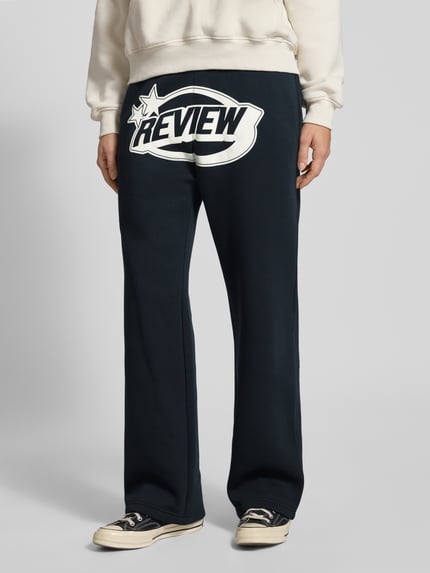 Frauenmodel trägt Straight Leg Sweatpants mit Logo und elastischem Bund von Review in Dunkelblau mit weißem Schriftzug, Baumwoll-Mix; Ganzkörperansicht von vorne.