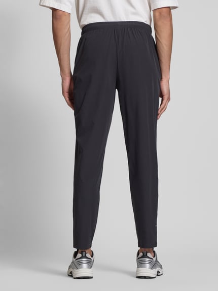 Männermodel trägt spodnie typu track pants z elastycznym pasem, model 'EVARO' od Ellesse, mieszanka materiałów z dodatkiem streczu, krój regular fit, długość wewnętrzna nogawki w rozmiarze M: 74 cm, kolor ciemnoszary, matowa tekstura, całkowity widok sylwetki z tyłu.