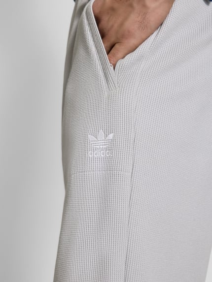 Männermodel trägt Straight Fit Sweatpants mit Strukturmuster Modell 'Essentials' von adidas Originals in Hellgrau, Nahaufnahme Oberschenkel.