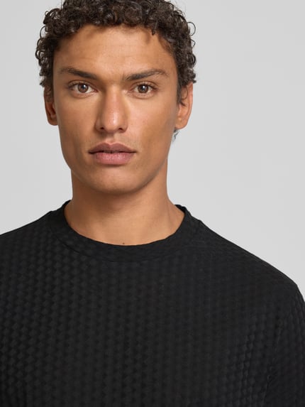 Männermodel trägt T-Shirt mit geripptem Rundhalsausschnitt von Emporio Armani, Reine Baumwolle, Regular-Fit, Label-Stitching, Nahaufnahme Oberkörper.