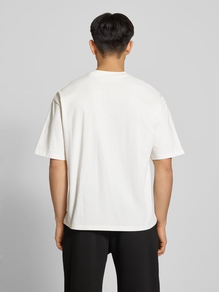 Männermodel trägt T-Shirt mit Label-Stitching und Rundhalsausschnitt von REVIEW, Relaxed-Fit, Reine Baumwolle, Rückenlänge 70 cm, Ganzkörperansicht Rückansicht.