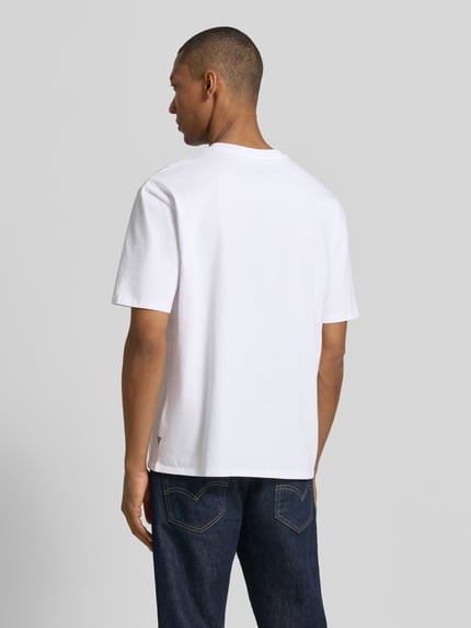 Männermodel trägt T-Shirt mit Motiv-Print und Rundhalsausschnitt von Guess aus reiner Baumwolle im Regular-Fit, Rückenlänge 68 cm, Ganzkörperansicht Rückansicht.