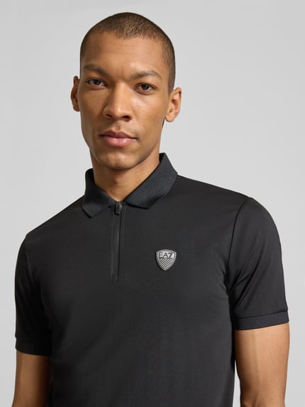 Männermodel trägt Slim Fit Poloshirt aus Viskose-Mix von EA7 Emporio Armani in Schwarz mit Logo-Detail, Nahaufnahme Oberkörper.