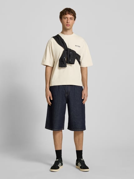 Mannenmodel draagt T-shirt met Label-Detail van REVIEW in crème, puur katoen, los model, ronde hals, 1/2-mouwen, ruglengte maat M 66 cm, geheellichaamsaanzicht van voren.