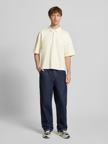 Männermodel trägt Regular Fit T-Shirt mit Polo-Kragen von adidas Originals in Creme, reine Baumwolle, dezentes Logo-Stitching, Ganzkörperansicht von vorne.