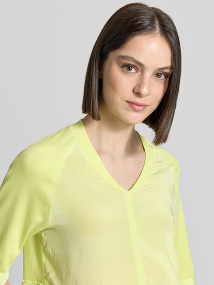 Frauenmodel trägt T-Shirt mit V-Ausschnitt und 3/4-Arm von Marc Cain in Gelb, Baumwoll-Elasthan-Mix, Relaxed-Fit, Nahaufnahme Oberkörper. Rückenlänge bei Größe 36: 60 cm.