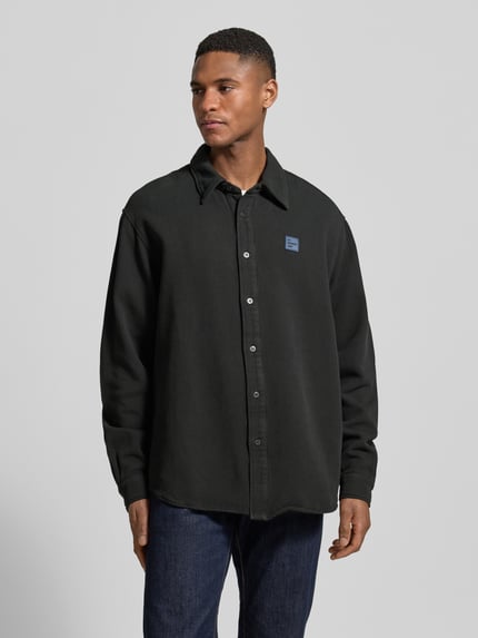 Männermodel trägt Regular Fit Freizeithemd mit Label-Patch von American Vintage in Schwarz, reine Baumwolle, Kentkragen, Knopfleiste, Ganzkörperansicht von vorne.